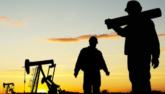 A view of oil workers at Well Pumpjack Site at dusk