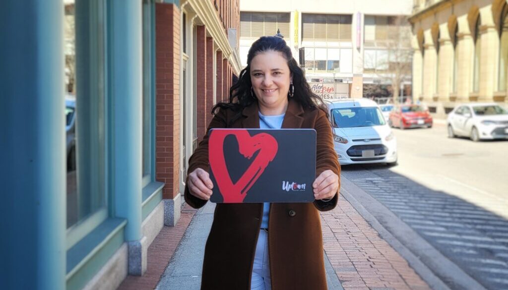 Shelley DeMerchant, owner of The Urban Shoe Myth in Saint John, holds up a novelty look of the new Uptown Saint John Gift Card. (Image: submitted)