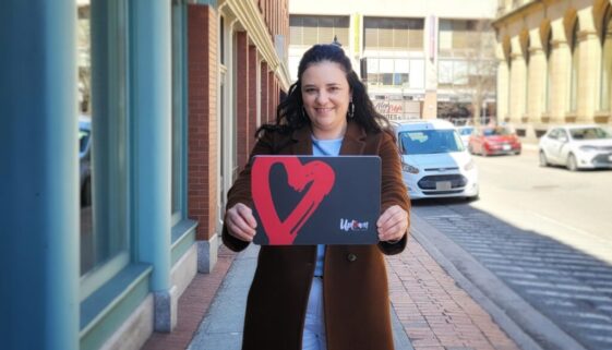 Shelley DeMerchant, owner of The Urban Shoe Myth in Saint John, holds up a novelty look of the new Uptown Saint John Gift Card. (Image: submitted)